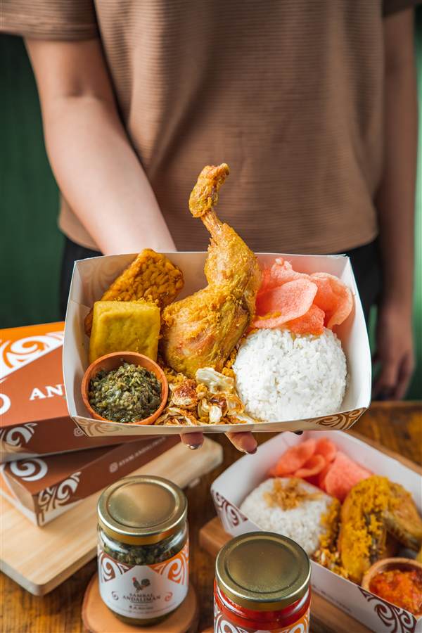 Rice box with fried chicken held up over branded packaging, Ayam Andaliman