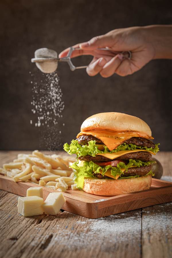 Salt sprinkled over a double cheeseburger on a wooden board