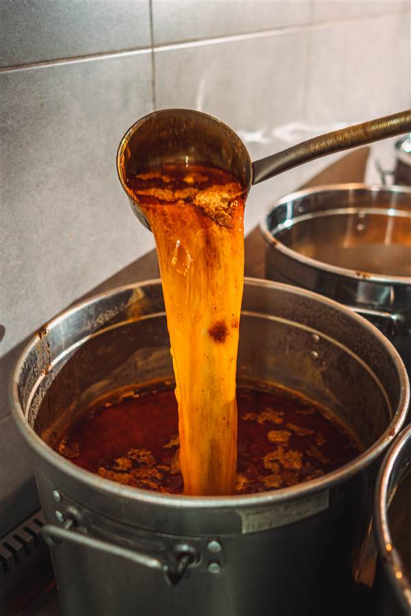Spicy broth poured from a ladle into a steel pot, Dragon Hotpot