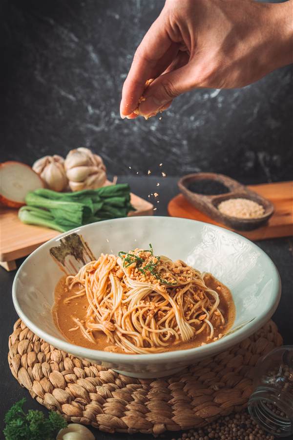 Hand sprinkling seasoning over noodles in a ceramic bowl, Feng Fu