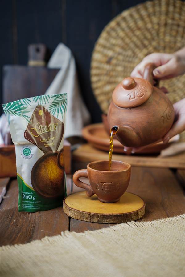 Tea poured from a clay pot beside palm sugar packaging, Gulare