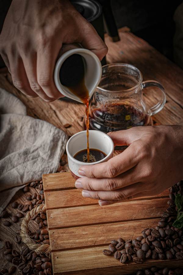 Hands pouring manual brew coffee into a cup on wooden crate, OTSS